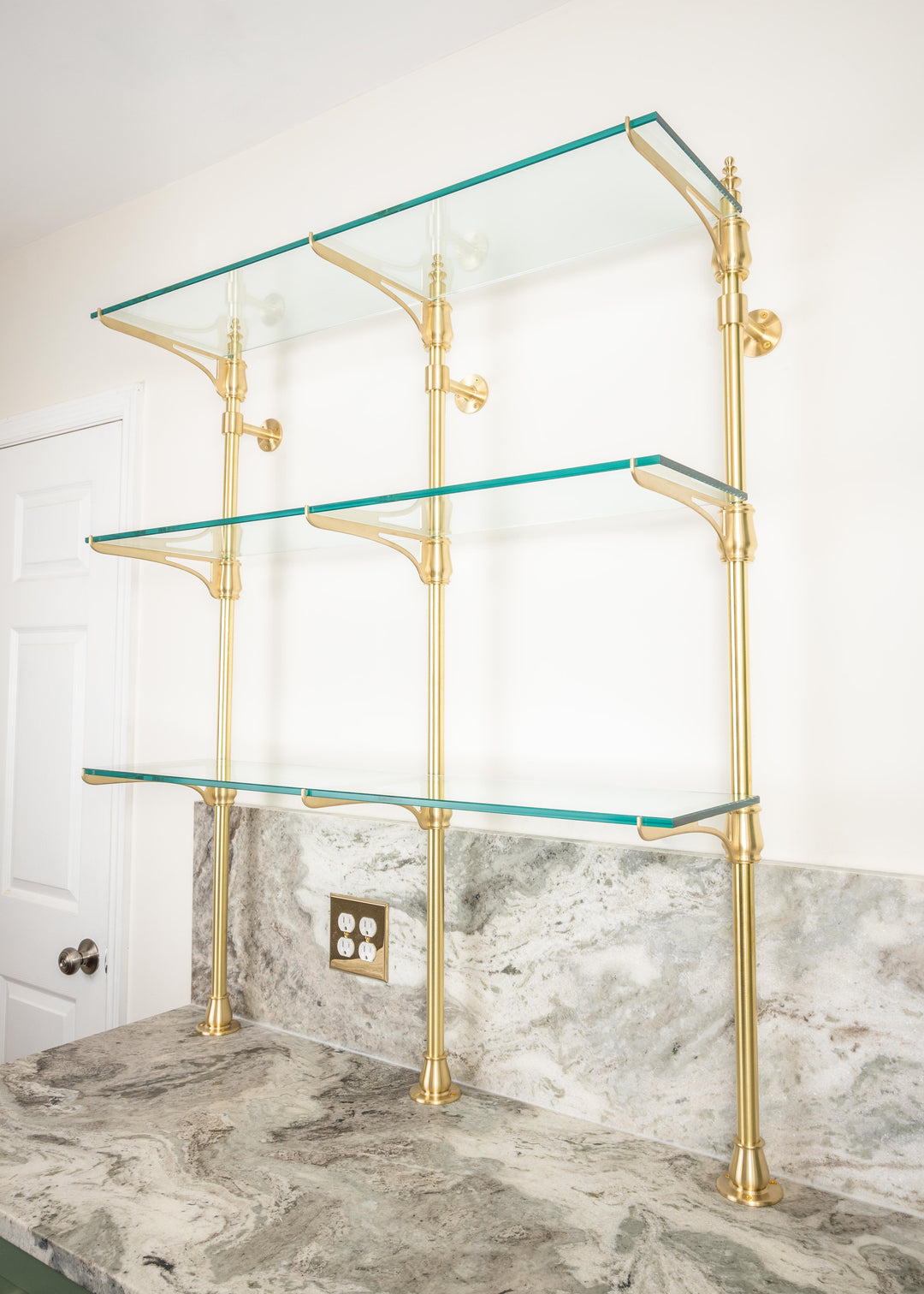 A customizable cantilever bistro shelving unit made from real brass with glass shelves that is mounted to the wall and countertop.