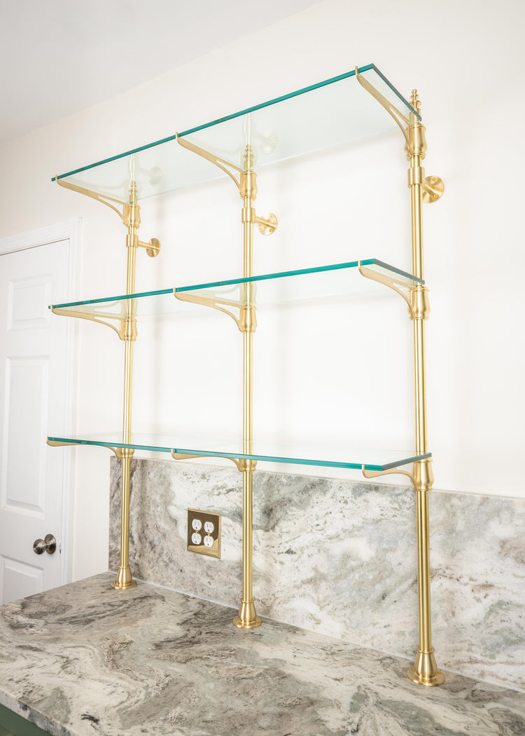 A customizable cantilever bistro shelving unit made from real brass with glass shelves that is mounted to the wall and countertop.