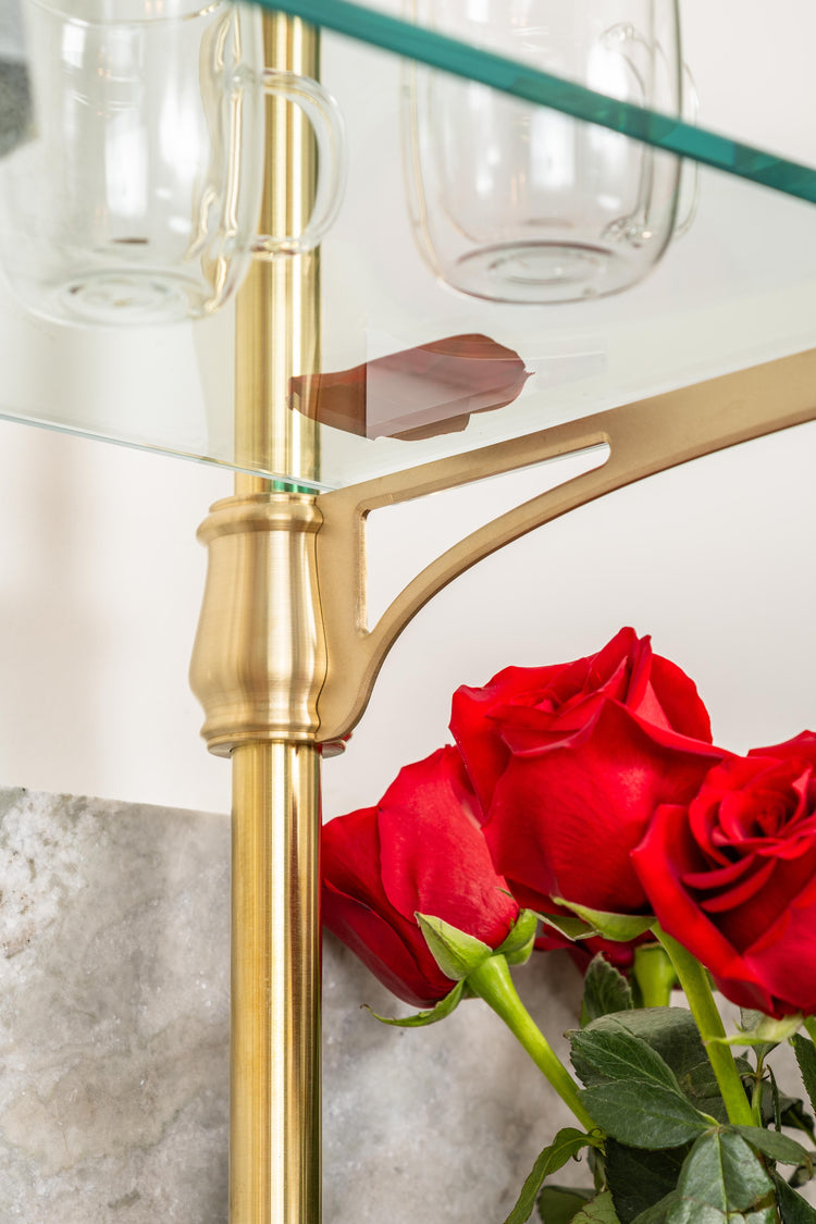 An ornate cantilever arm of a bistro shelving unit made from real brass that is supporting a glass shelf.