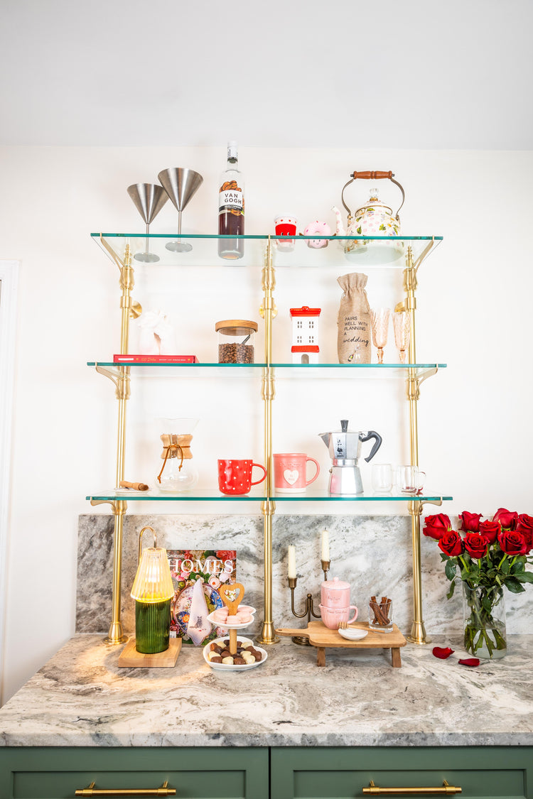 A brass cantilever bistro shelving unit mounted on the wall and counter being used as a coffee bar.